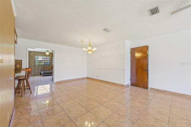 tiled spare room with ceiling fan with notable chandelier and a textured ceiling