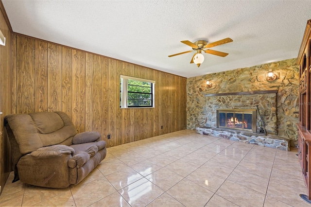 sitting room with ceiling fan, light tile floors, a stone fireplace, and wooden walls