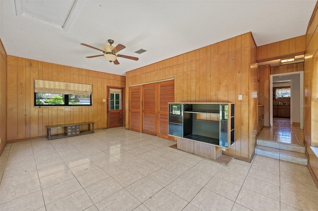 unfurnished living room with wood walls, ceiling fan, and light tile floors