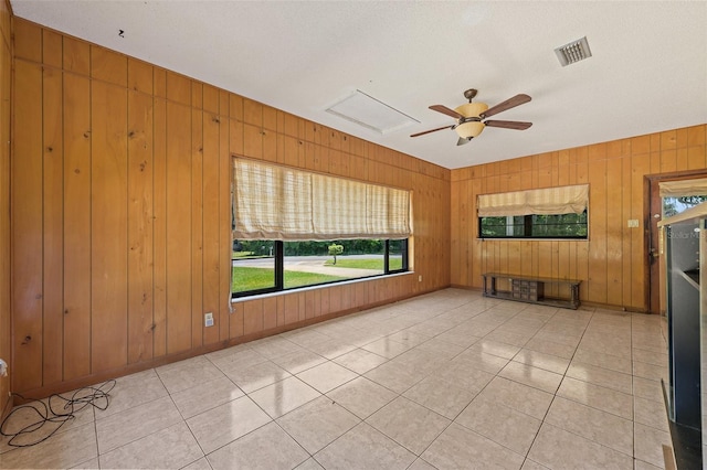 empty room with wooden walls, a textured ceiling, ceiling fan, and light tile floors