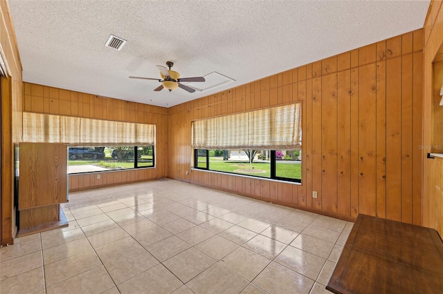 tiled spare room with a textured ceiling, ceiling fan, and wooden walls