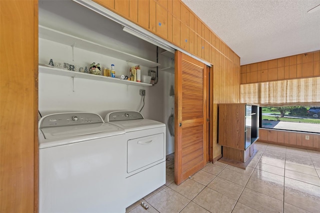 washroom with light tile flooring, wood walls, a textured ceiling, and washer and dryer