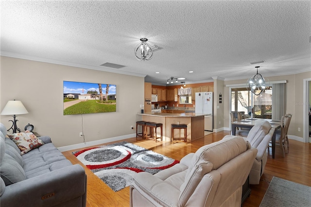 living room featuring a chandelier, light hardwood / wood-style floors, a textured ceiling, and crown molding