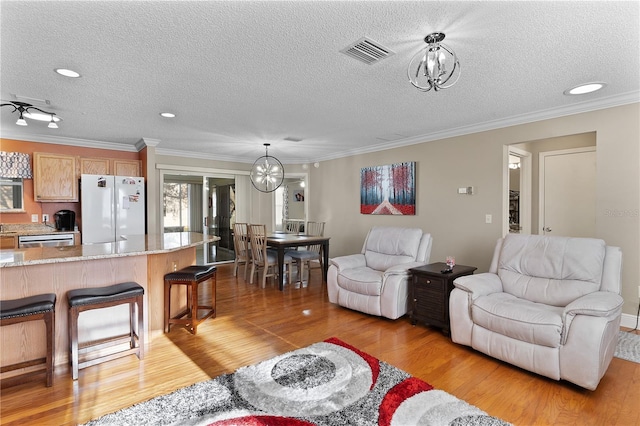 living room with crown molding, an inviting chandelier, a textured ceiling, and light hardwood / wood-style flooring