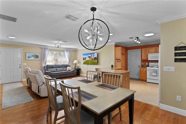 dining space with a notable chandelier, light wood-type flooring, ornamental molding, and a textured ceiling