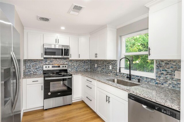 kitchen with stainless steel appliances, white cabinetry, sink, and light stone counters