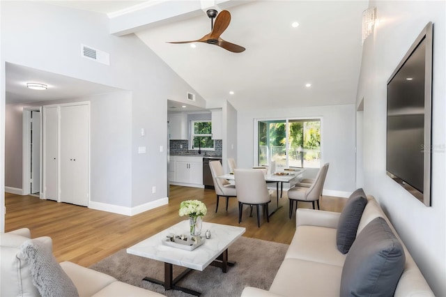 living room with hardwood / wood-style flooring, high vaulted ceiling, beam ceiling, and sink