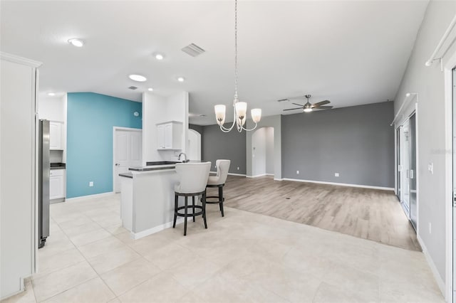 kitchen featuring hanging light fixtures, ceiling fan with notable chandelier, white cabinetry, a kitchen breakfast bar, and light tile floors