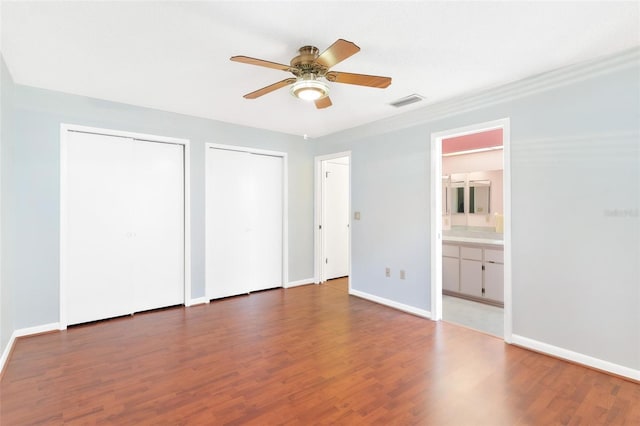 unfurnished bedroom with connected bathroom, multiple closets, ceiling fan, and dark hardwood / wood-style floors