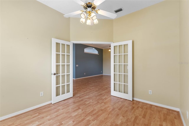 empty room featuring french doors, ceiling fan, a high ceiling, and light wood-type flooring