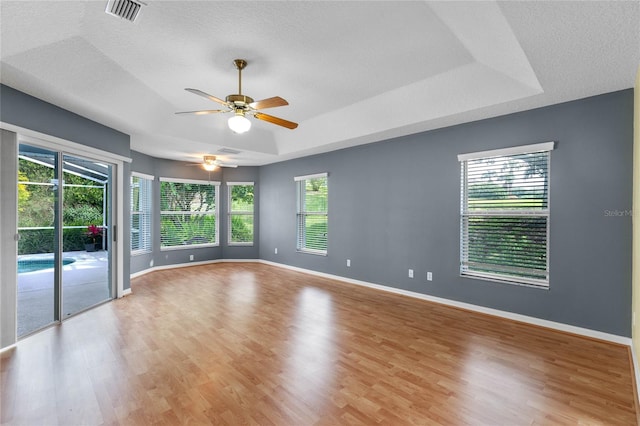 unfurnished room with light hardwood / wood-style floors, ceiling fan, a textured ceiling, and a tray ceiling