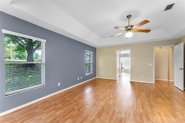 unfurnished room with light wood-type flooring, ceiling fan, and a tray ceiling