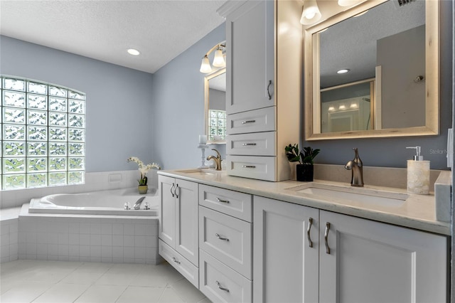 bathroom with tile flooring, double sink vanity, a textured ceiling, and tiled tub