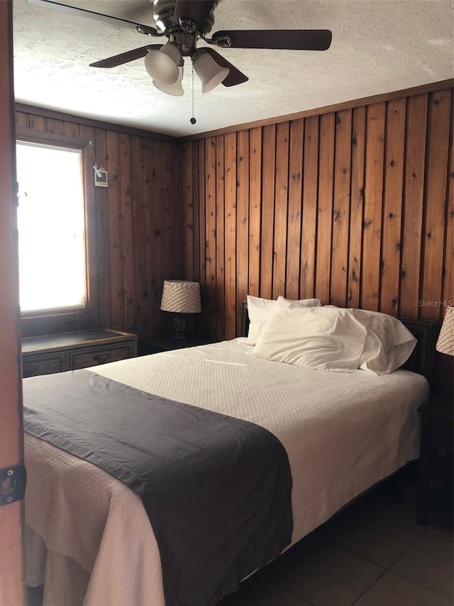 bedroom with wooden walls, tile flooring, ceiling fan, and a textured ceiling