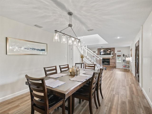 dining space with brick wall, light wood-type flooring, and a fireplace