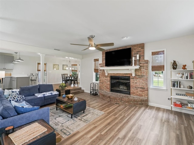 living room featuring ceiling fan, a brick fireplace, hardwood / wood-style floors, brick wall, and ornate columns