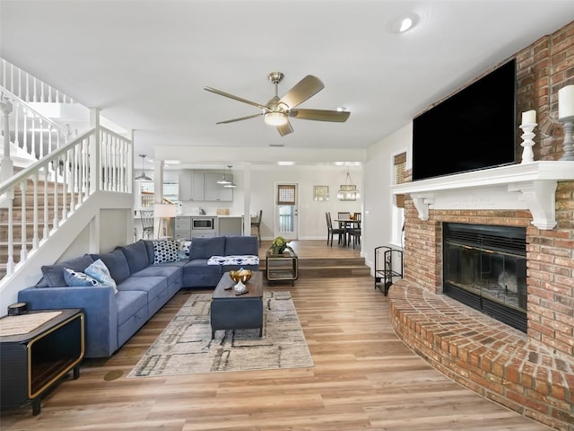 living room featuring ceiling fan, light hardwood / wood-style floors, brick wall, and a brick fireplace