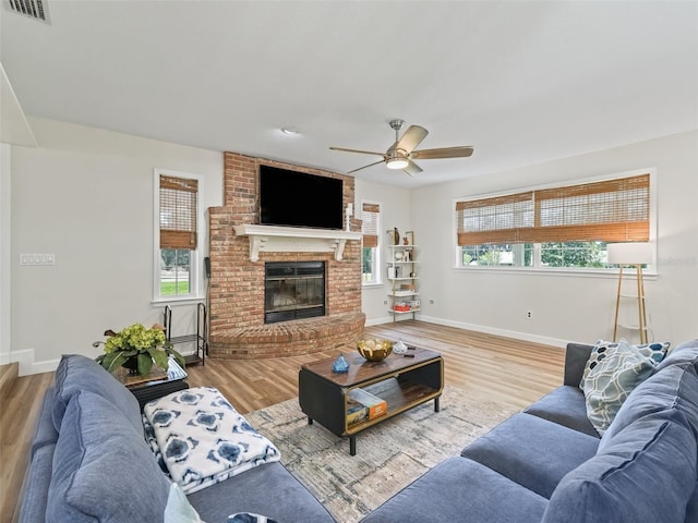 living room with light hardwood / wood-style flooring, ceiling fan, a fireplace, and plenty of natural light