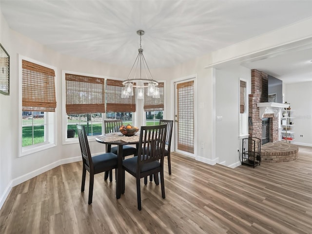 dining area with a fireplace, hardwood / wood-style floors, a notable chandelier, and brick wall