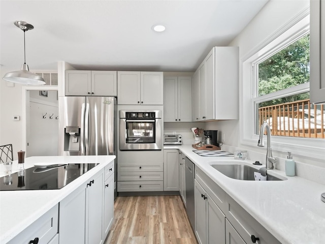 kitchen with appliances with stainless steel finishes, gray cabinets, sink, pendant lighting, and light wood-type flooring