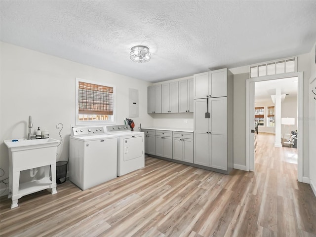 clothes washing area featuring cabinets, light hardwood / wood-style floors, a textured ceiling, and washer and clothes dryer