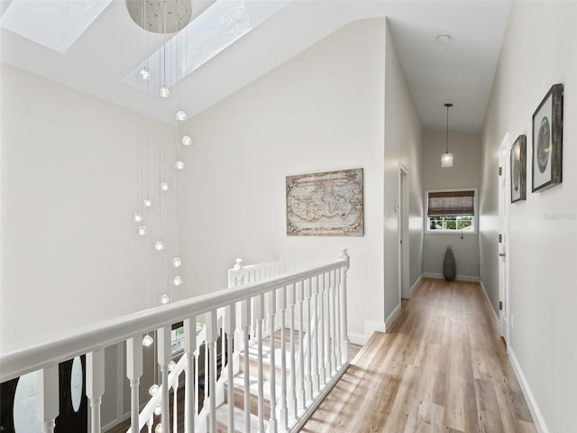 hall featuring a skylight, high vaulted ceiling, and light hardwood / wood-style floors