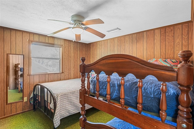 carpeted bedroom featuring wooden walls, ceiling fan, and a textured ceiling