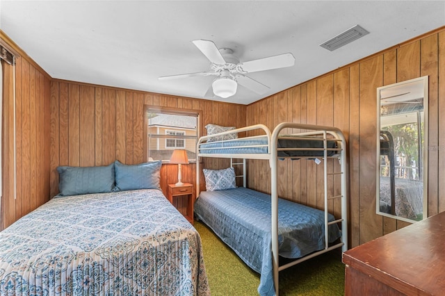 carpeted bedroom with wood walls, ceiling fan, and multiple windows