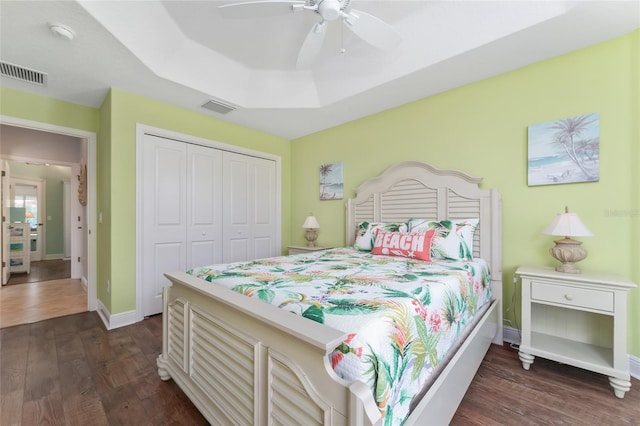 bedroom with ceiling fan, a closet, dark hardwood / wood-style floors, and a raised ceiling