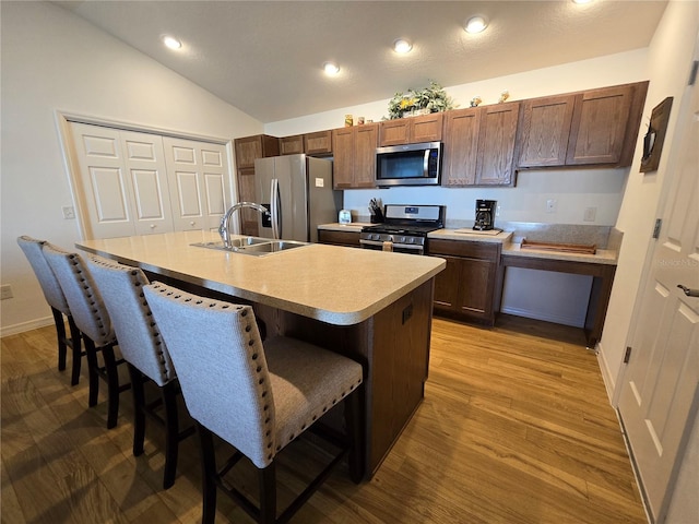 kitchen with appliances with stainless steel finishes, a kitchen island with sink, sink, hardwood / wood-style floors, and a kitchen breakfast bar