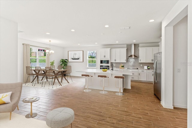 kitchen featuring appliances with stainless steel finishes, wall chimney exhaust hood, tasteful backsplash, a breakfast bar area, and a center island with sink