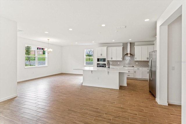 kitchen with a kitchen bar, backsplash, black appliances, wall chimney range hood, and an island with sink