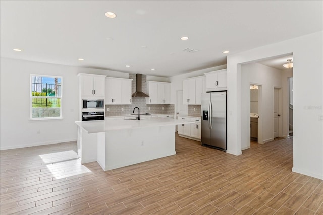 kitchen featuring stainless steel refrigerator with ice dispenser, wall oven, built in microwave, wall chimney range hood, and a center island with sink