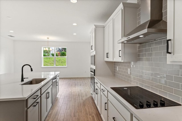 kitchen with backsplash, stainless steel appliances, light hardwood / wood-style floors, wall chimney range hood, and sink