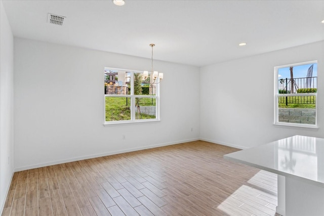 empty room with light wood-type flooring and an inviting chandelier