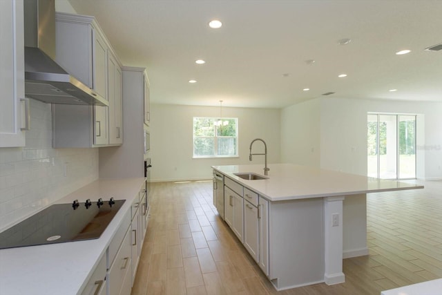 kitchen with sink, an island with sink, wall chimney exhaust hood, and a wealth of natural light