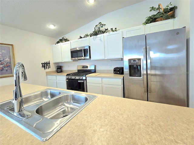 kitchen with appliances with stainless steel finishes, white cabinets, sink, and lofted ceiling