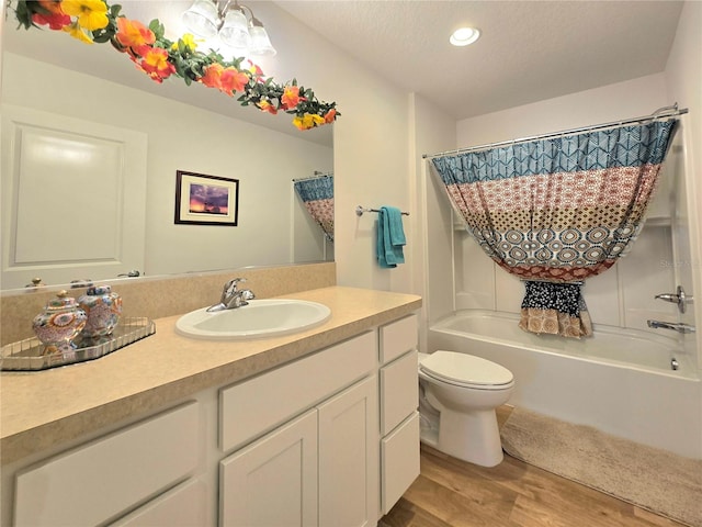 full bathroom featuring toilet, shower / bath combo with shower curtain, wood-type flooring, a textured ceiling, and vanity