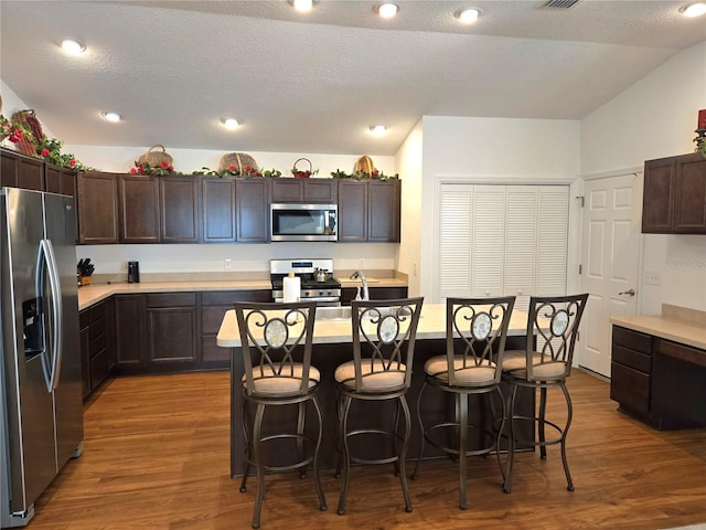 kitchen featuring a breakfast bar, hardwood / wood-style floors, appliances with stainless steel finishes, dark brown cabinets, and an island with sink