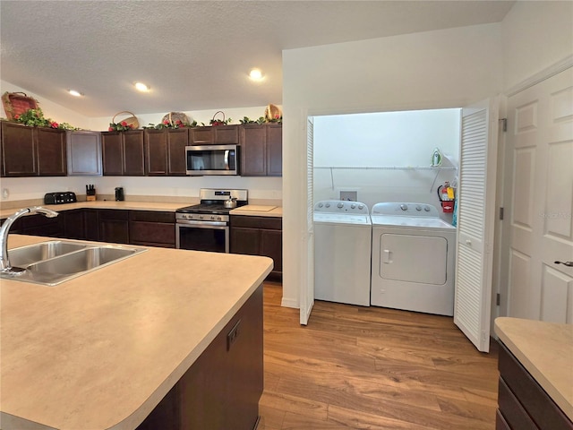 kitchen with sink, appliances with stainless steel finishes, washer and dryer, dark brown cabinetry, and light wood-type flooring