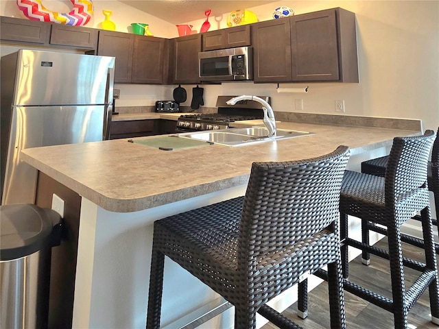 kitchen featuring kitchen peninsula, sink, a kitchen bar, appliances with stainless steel finishes, and dark brown cabinetry