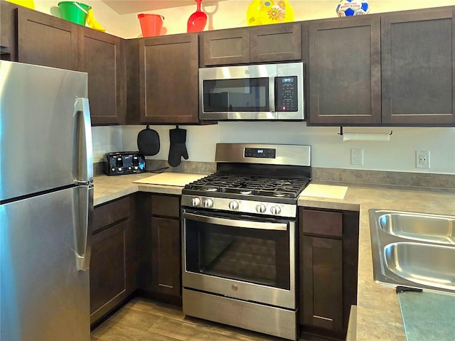 kitchen with light hardwood / wood-style floors, stainless steel appliances, dark brown cabinetry, and sink