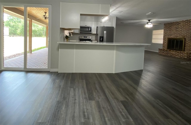 kitchen with kitchen peninsula, stainless steel appliances, dark hardwood / wood-style floors, and a brick fireplace