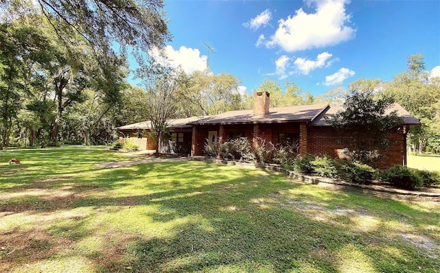 back of house with brick siding, a lawn, and a chimney