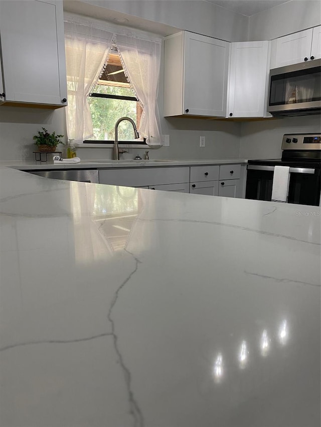 kitchen featuring light stone countertops, appliances with stainless steel finishes, and white cabinetry