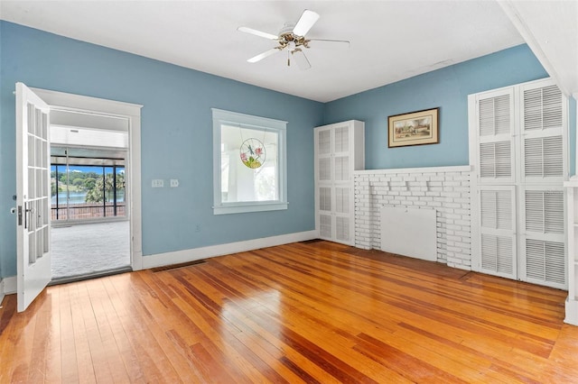 unfurnished room featuring a fireplace, light wood-type flooring, and ceiling fan