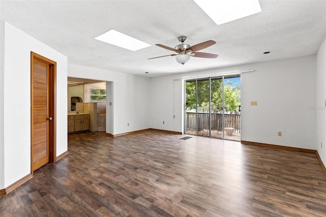 empty room with a textured ceiling, a skylight, ceiling fan, and dark hardwood / wood-style floors