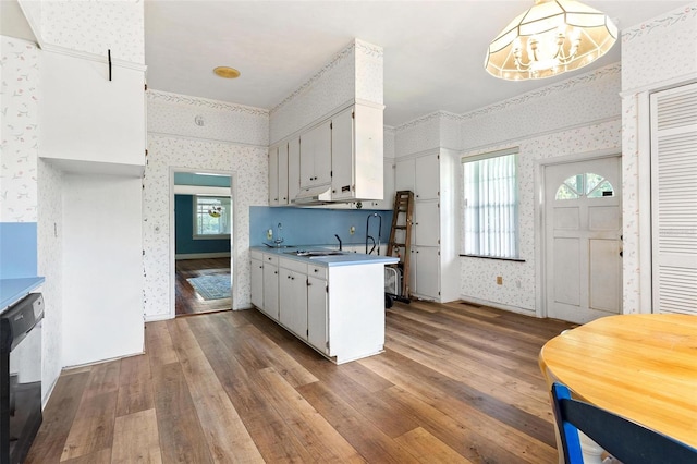 kitchen with sink, a chandelier, hardwood / wood-style floors, black dishwasher, and white cabinetry