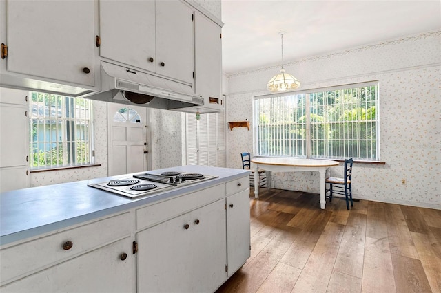 kitchen with white stovetop, pendant lighting, wood-type flooring, white cabinets, and a chandelier