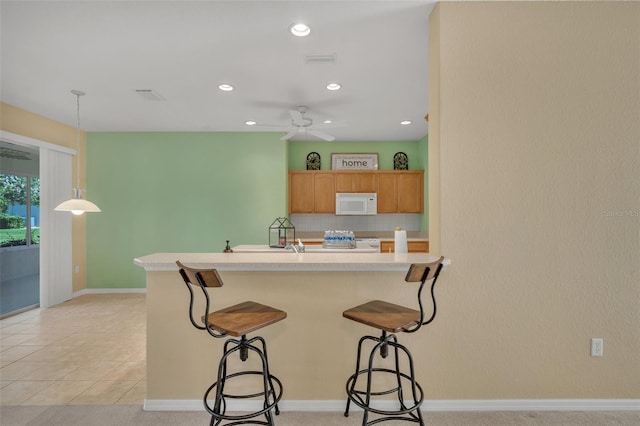 kitchen featuring hanging light fixtures, a breakfast bar area, ceiling fan, light tile flooring, and range